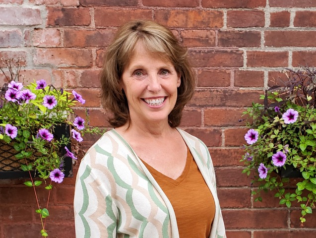 Beth Rosener smiling in front of a brick wall and flowering plants.
