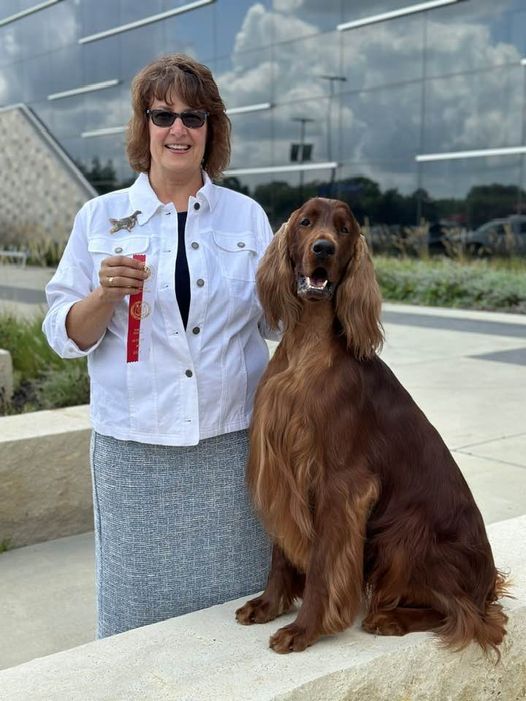 Sarah Schroeder standing with an Irish Setter and holding a show-ring ribbon.